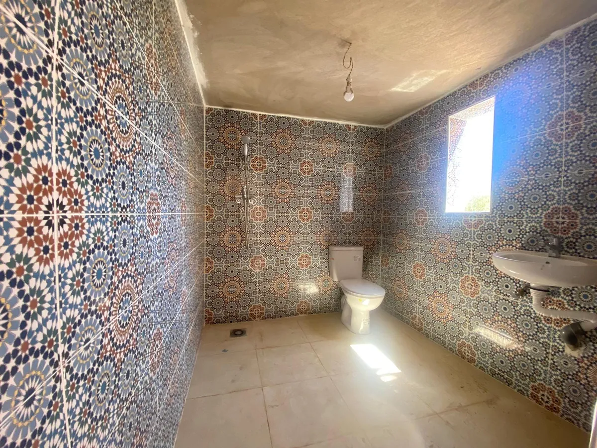 Une salle d'eau dont les murs sont entièrement couverts de zelliges à motifs, avec lavabo et douche.