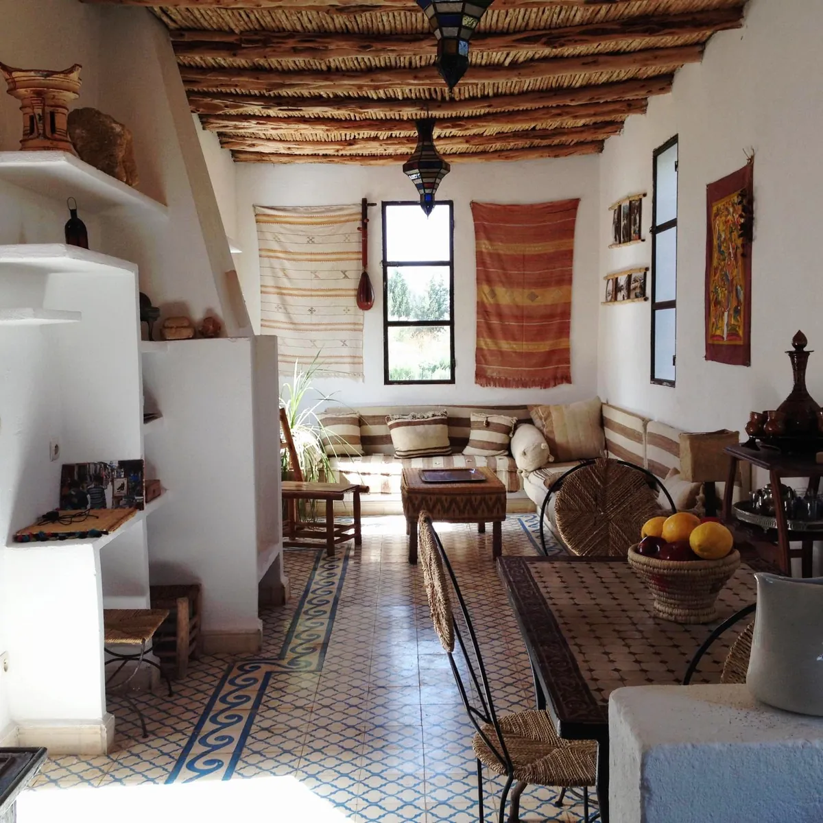 Une pièce à vivre au plafond de roseaux et de bois, avec une banquette, une table en zellige et des tissages aux murs.